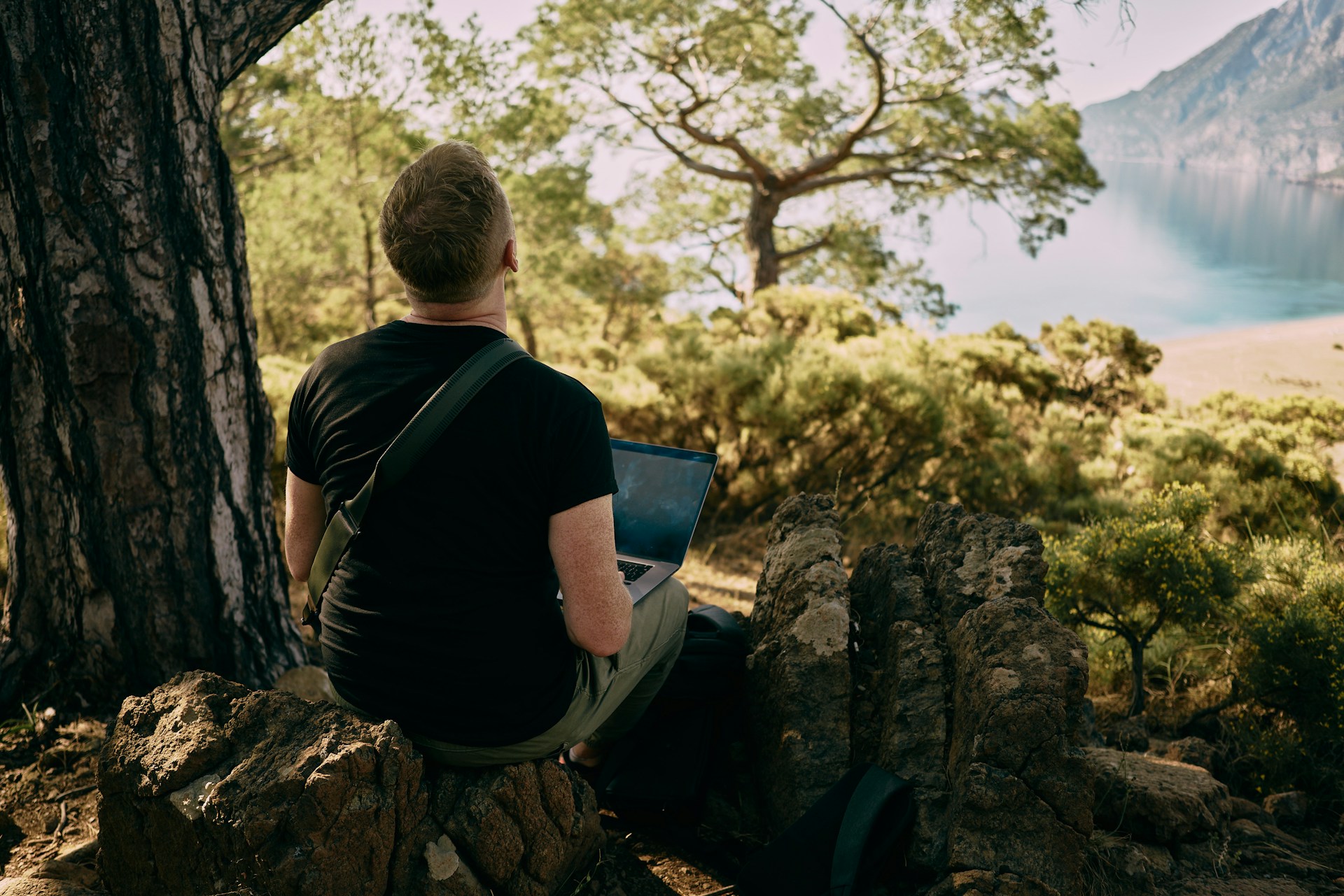 Man sitting on a rock with a laptop, enjoying the view